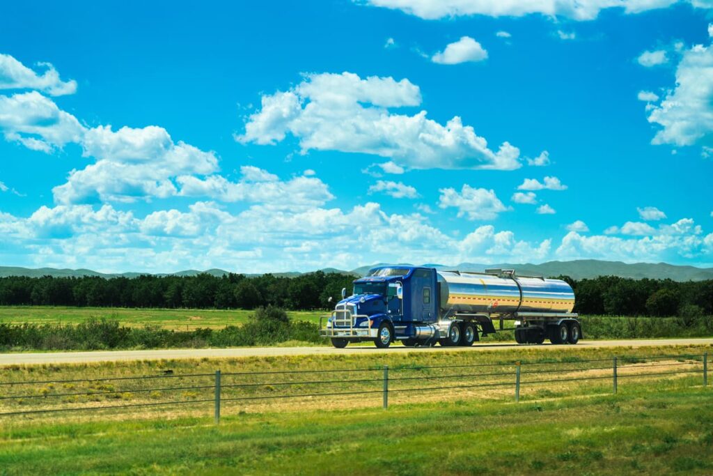 Fuel tanker semi-truck driving on the highway with blue sky and grass in the background